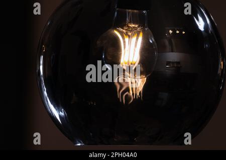Round glass lampshade with a tungsten lamp inside glowing in the dark, close-up photo with selective soft focus Stock Photo