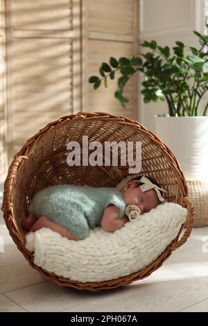Adorable newborn baby with pacifier sleeping in overturned wicker basket at home Stock Photo