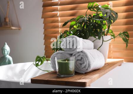Soft towels, burning candle and green plant on bathtub in room. Interior design Stock Photo