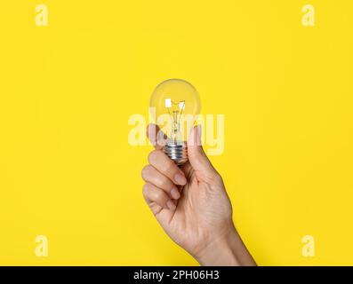 Woman holding incandescent light bulb on yellow background, closeup Stock Photo