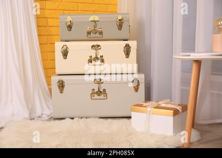 Storage trunks and gift box near yellow brick wall indoors. Interior design Stock Photo