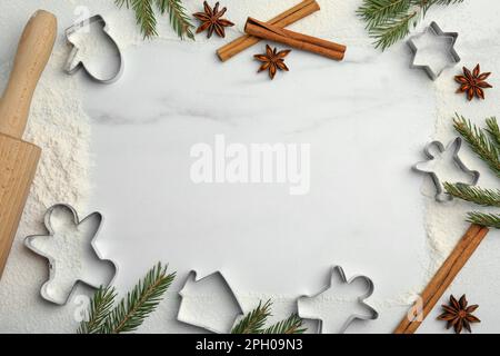 Frame of cookie cutters, cinnamon sticks, flour and anise stars on white marble table, flat lay. Space for text Stock Photo