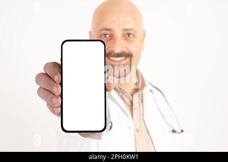 Caucasian male doctor showing smartphone. Big blank empty white screen for mockup. Isolated white background, copy space. Stock Photo