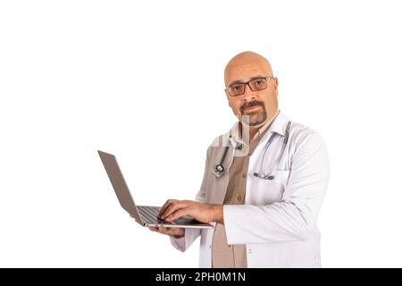 Portrait of bald middle aged handsome bearded doctor using laptop. Millennial caucasian male physician wearing glasses and looking camera, holding pc. Stock Photo