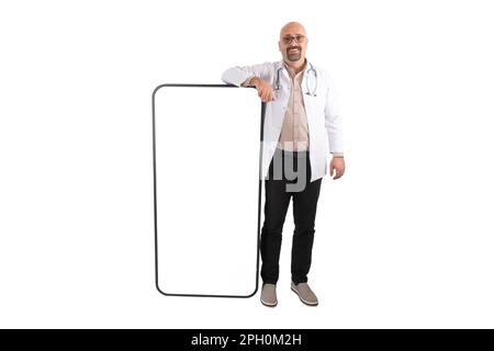 Middle aged caucasian European doctor leaning big smartphone. Isolated white background. Empty screen of mobile phone mock up. Medical mobile app. Stock Photo