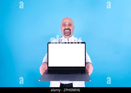 Portrait of happy smiling middle aged bald caucasian man holding laptop. Showing empty white screen notebook for mock up. Excited doctor offering. Stock Photo