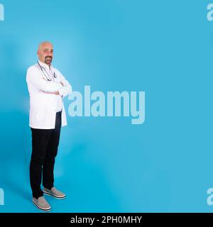 Portrait of trusted middle aged male doctor. Physician in white coat with stethoscope, arms crossed on chest over blue background square image. Stock Photo