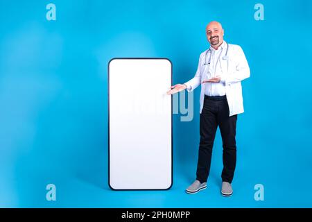 Caucasian man standing near big blank cellphone for mobile offer concept. Doctor showing huge smartphone with his hands. White empty screen for mockup Stock Photo