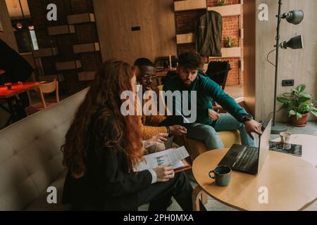 Three young programmers looking for a solution at their code while working together remotely at the coffee bar. Male person pointing at lap top Stock Photo