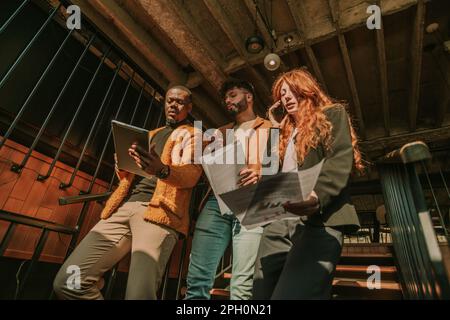 Gorgeous redhead businesswoman having a phone call while her two male multiracial colleagues are discussing something on the tablet. They are walking Stock Photo