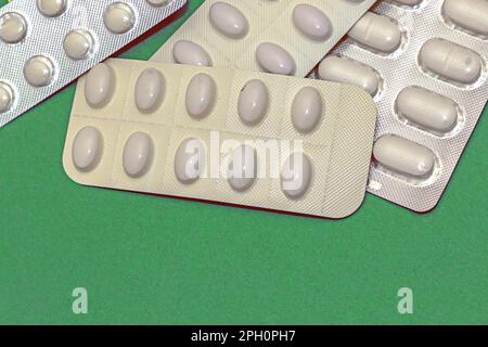 Pile of medical pills in white blisters packaging isolated on green background Stock Photo