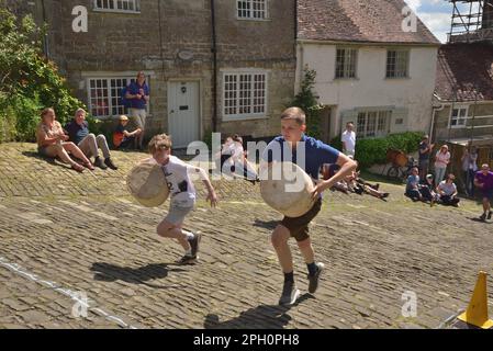 Two boys carry their 'cheeses' in the cheese race running up Gold Hill, Shaftesbury, during the town's Food and Drink Festival on 8th May 2022. Stock Photo