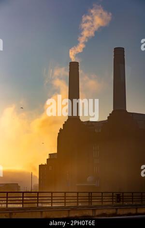 A smoking chimney on the silhouetted Battersea Power Station at dawn Stock Photo