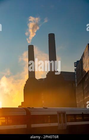 A smoking chimney on the silhouetted Battersea Power Station at dawn Stock Photo