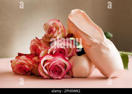 new ballet slippers lying on pink background with roses. elegant ballet shoes bouquet. beauty dance Stock Photo