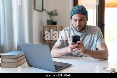 Surprised man with wide opened eyes looking at screen of mobile phone. Stock Photo