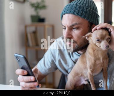 Man sitting at home with his little dog and using his smart phone. Stock Photo