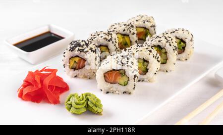 Sushi roll California with salmon, sesame seeds, avocado, cream cheese on white background. Sushi menu, rolls served on white dish and soy sauce. Trad Stock Photo