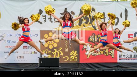 Group of young Japanese women in skimpy cheerleader costumes on an outdoor stage performing Yosakoi dancing at the annual Kumamoto Kyusyu gassai dance festival, itself part of the Spring Festival. Dancers caught jumping in mid-air. Stock Photo