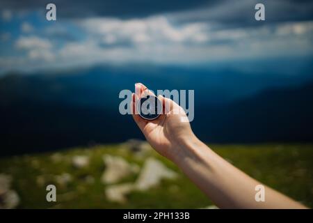 Traveler woman hand holds a hand-held compass against the backdrop of mountains and hills at sunset. The concept of travel and navigation in open Stock Photo