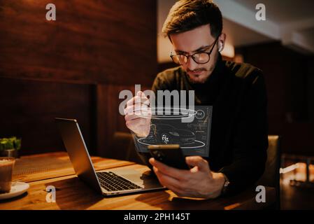 An engineer using a smarpthone in a cafe while viewing a hologram of the automotive industry. HUD of the automotive industry Stock Photo