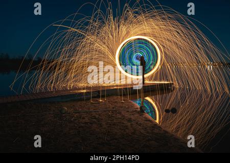 Burning steel wool spinned in urban area. Showers of glowing sparks from spinning steel wool. Man in the fire. Stock Photo