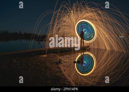 Burning steel wool spinned in urban area. Showers of glowing sparks from spinning steel wool. Man in the fire. Stock Photo