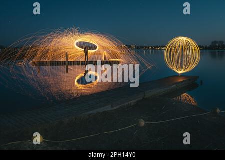 Burning steel wool spinned in urban area. Showers of glowing sparks from spinning steel wool. Man in the fire. Stock Photo