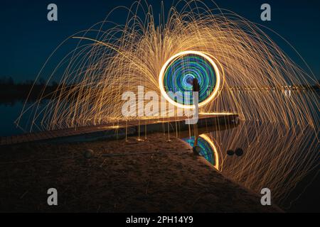 Burning steel wool spinned in urban area. Showers of glowing sparks from spinning steel wool. Man in the fire. Stock Photo