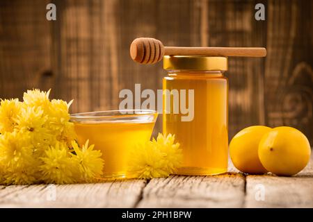 Honey in a glass jar and bowl, wooden dipper, lemon, yellow flowers on a wooden background. The concept of organic food. Stock Photo