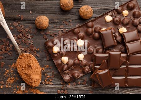Handmade chocolate with hazelnuts, dark chocolate pieces, cocoa in a vintage spoon, chocolate truffles on a dark wooden background top view. Stock Photo