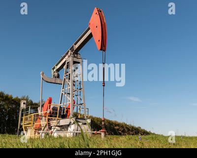 Operating oil and gas well in oil field, profiled against the blue sky. Stock Photo