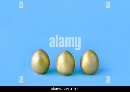 Easter eggs on blue background. Three golden eggs. Minimal style. Easter decorations. Happy Easter. Stock Photo