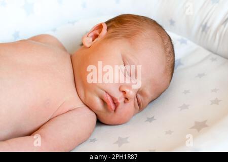 Closeup portrait of Newborn baby sleeping on white blanket. Soft focus. A one weeks old infant is sleeping tightly on her side in bed. 10 days old chi Stock Photo