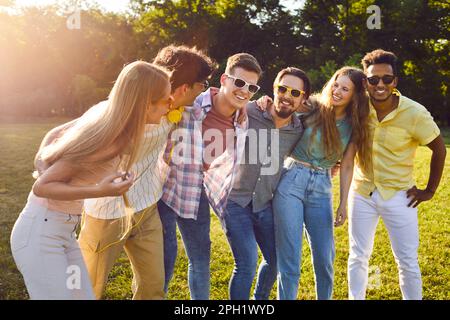 Six happy young friends hugging, laughing and having fun in park on sunny day while walking. Stock Photo