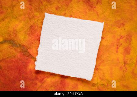 small square sheet of blank white Khadi paper against colorful marbled paper Stock Photo