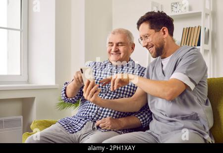 Smiling senior man and caregiver doing video call using smartphone Stock Photo