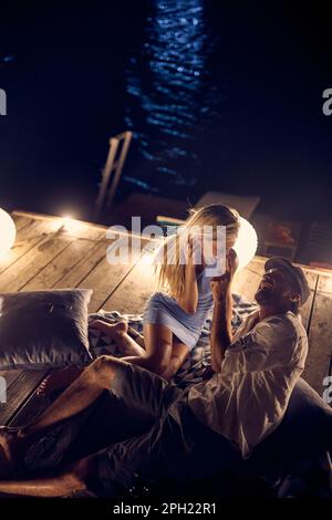 Couple having fun on date night. Young man and woman on wooden jetty having romantic date. Love, togetherness, fun, lifestyle concept. Stock Photo
