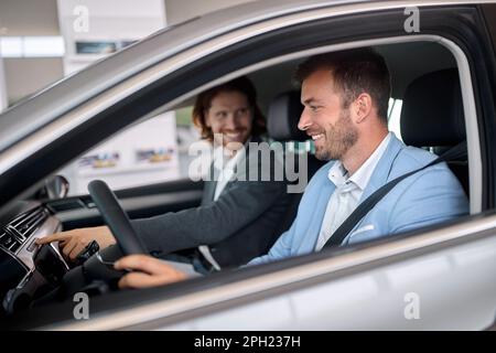 Male buyer with salesman trying new car in selling salon Stock Photo