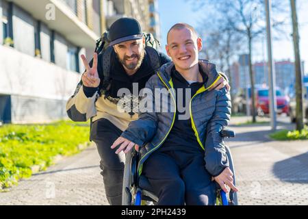 A young man in a wheelchair with his companion posing for the camera on a sunny day Stock Photo