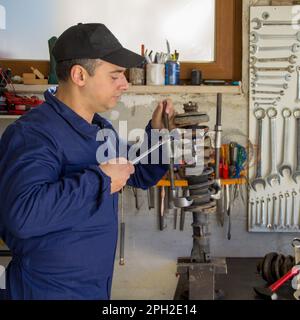 Image of a mechanic in overalls in his workshop while he disassembles a car shock absorber with a wrench and extractors. Stock Photo