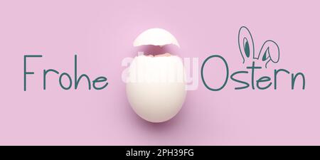 Cracked egg shell and text FROHE OSTERN (Happy Easter in German) on lilac background Stock Photo