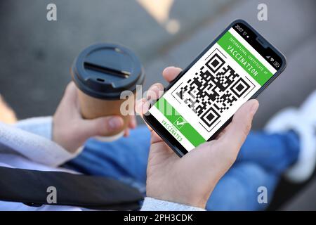 Man holding smartphone with international certificate of vaccination outdoors, closeup Stock Photo