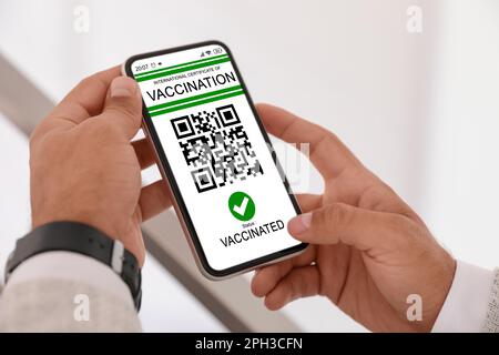 Man holding smartphone with international certificate of vaccination indoors, closeup Stock Photo