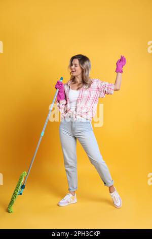 Beautiful young woman with mop singing on orange background Stock Photo