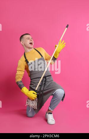 Handsome young man with mop singing on pink background Stock Photo