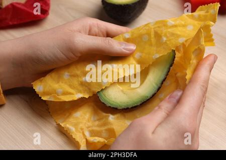 Woman packing half of fresh avocado into beeswax food wrap at wooden table, closeup Stock Photo