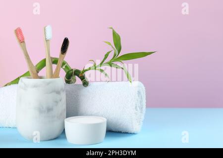 Bamboo toothbrushes, towel and bowl of baking soda on light blue table against pink background, space for text Stock Photo