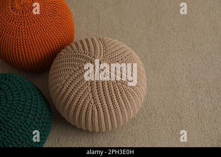 Different stylish knitted poufs on carpet indoors, space for text Stock Photo