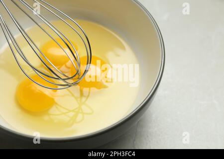 Whisking eggs in bowl on light grey table, closeup Stock Photo